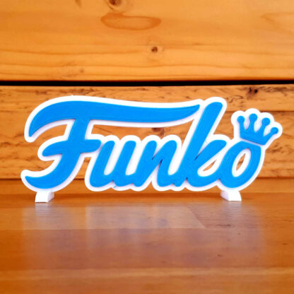 Logo 3D Funko bleu clair posé sur son socle, sur un plan de travail en bois